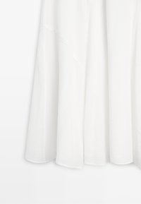 White flowing fabric with soft pleats and a slightly sheer texture, hanging straight with subtle layered details.