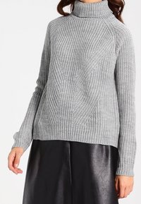 Maglione grigio a collo alto lavorato a maglia con texture a coste, caratterizzato da una vestibilità ampia e maniche lunghe, abbinato a una gonna in pelle nera.