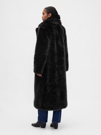 Manteau en fausse fourrure noire avec col montant, manches longues et coupe ample, présentant une surface douce et texturée, et une longueur sous le genou.