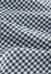 Navy- und weißes Gingham-Gewebe mit einem kleinen Karomuster, das eine glatte Textur aufweist und durch gefaltete Abschnitte Tiefe erzeugt.