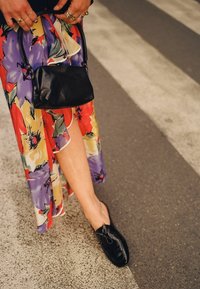 Scarpe in pelle nera con dettagli a fiocco, abbinate a una gonna a stampa floreale colorata che presenta tonalità di rosso, viola e giallo.