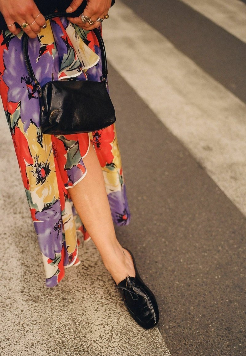 Scarpe in pelle nera con dettagli a fiocco, abbinate a una gonna a stampa floreale colorata che presenta tonalità di rosso, viola e giallo.