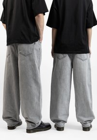 Light gray wide-leg denim pants with a high waist. Features two back pockets, subtle stitching details, and a relaxed silhouette. Black footwear.