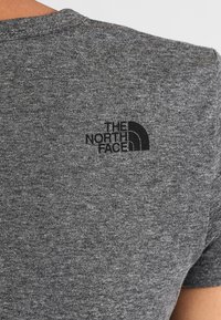 Szara koszulka z krótkim rękawem wykonana z teksturowanej tkaniny. Na górnej części pleców znajduje się czarne logo w celach promocyjnych.