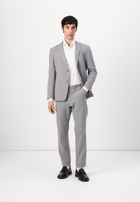 Light gray suit with a fitted design, single button blazer, and matching pants. Worn over a white shirt and paired with black shoes.