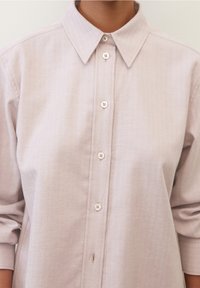 Camicia button-up rosa chiaro realizzata in tessuto testurizzato con motivo a spina di pesce, dotata di colletto classico e cinque bottoni sul fronte.