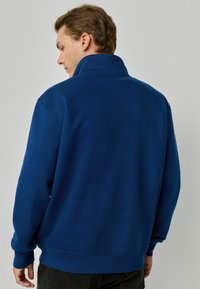Sudadera de forro polar azul marino con cuello alto, mangas largas y puños y dobladillo acanalados. Textura suave y diseño simple.