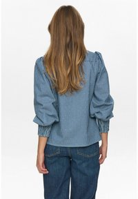 Zila un balta svītrainā blūze ar pūkainām piedurknēm un elastīgām aprocēm. Strukturēts audums ar brīvu piegriezumu, valkāts kopā ar ziliem džinsiem.