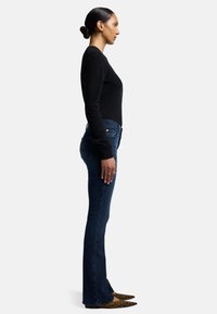 Svart åtsittande tröja och mörkblå utsvängda jeans. Jeans med femficksdesign. Bruna och svarta pumps med spetsig tå och leopardmönster.