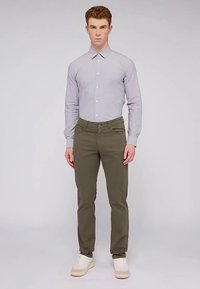 Camisa de manga larga gris claro con cuello y bolsillo en el pecho, combinada con pantalones ajustados de color verde oliva y zapatillas beige.