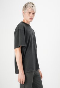 Black cotton t-shirt with short sleeves, a round neckline, and a chest pocket. Soft texture, oversized fit, and unfinished hems.