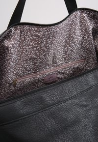 Borsa a tracolla nera in pelle con un esterno testurizzato. L'interno ha una fodera con motivo floreale in mauve e una tasca con zip rosa.