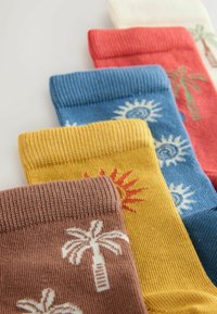 Quatre chaussettes tricotées colorées avec des motifs de soleil et de palmier en marron, jaune, bleu et rouge, disposées en chevauchement sur une surface blanche.