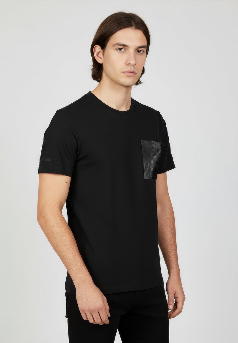 Black short-sleeve t-shirt made from smooth fabric, featuring a textured black pocket on the left chest and a logo on the sleeve.