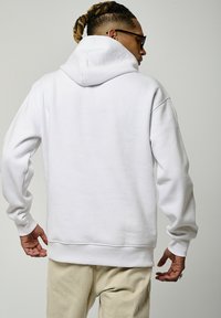 Hoodie blanc en tissu doux, doté d'une grande capuche, de manches longues et d'une coupe décontractée. Design simple et minimaliste sans motifs visibles.