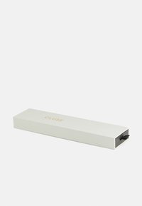 Boîte rectangulaire blanche avec surface texturée, logo "CLUSE" doré sur le dessus et une languette noire pour l'ouvrir. Convient pour l'emballage d'accessoires.
