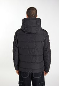 Sort pufferjakke med høj krave og horisontalt quiltet design. Har hætte og elastiske manchetter for varme og komfort.