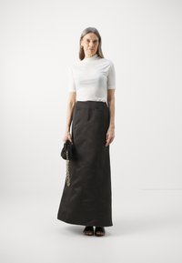 Hvit tettsittende topp med korte ermer, kombinert med en lang, mørkebrun skjørt. Modellen holder en svart veske med kjededetalj.