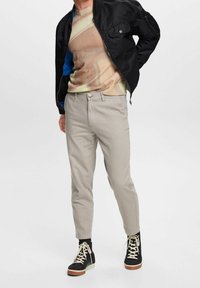 Szare spodnie o dopasowanym kroju, zestawione z wielokolorowym swetrem w abstrakcyjny wzór oraz czarną kurtką bomber. Na nogach czarne trampki.