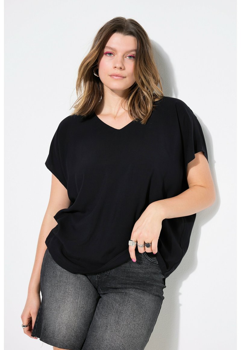 Zwarte, losvallende V-hals top gemaakt van zachte stof, met korte mouwen, gecombineerd met donkere, knielange denim shorts. Elegante draping en silhouet.