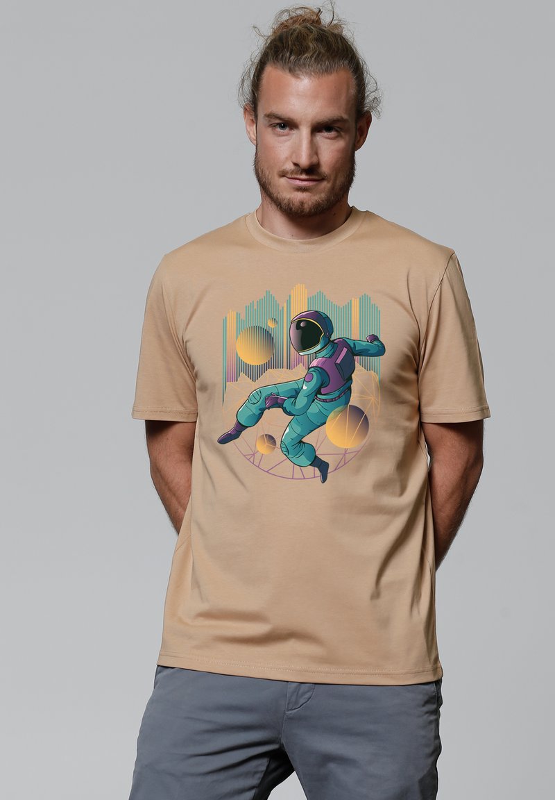 Beige T-shirt met een kleurrijke astronautafbeelding in turquoise en paars, met een gladde textuur en korte mouwen.
