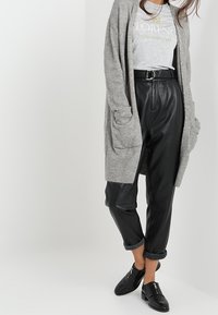 Grå stickad cardigan över en grå t-shirt med texten "FLORENCE". Svarta byxor i konstläder med uppvikta fållar och svarta ankelstövlar.