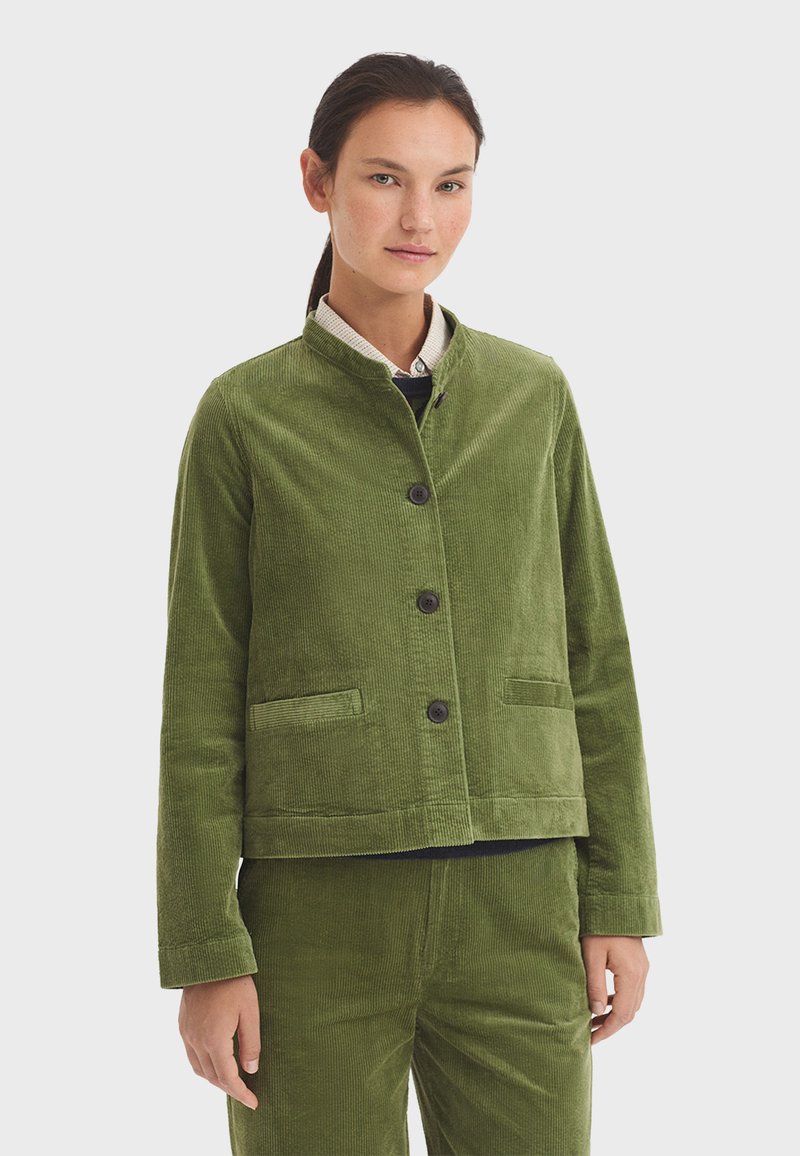 Giacca in cotone a coste verde con colletto alla mandarina, chiusura frontale con bottoni e due tasche laterali. Tessuto testurizzato e design accorciato.