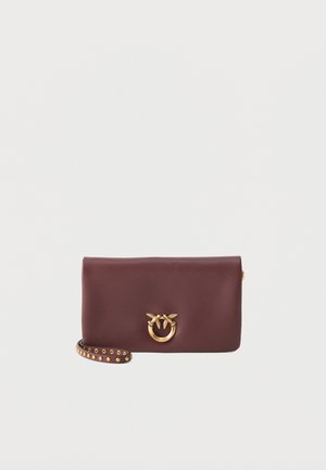 Pochette en cuir marron foncé avec fermoir circulaire doré orné de deux oiseaux, et une sangle en cuir cloutée pour le poignet.