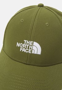 Zöld sapka struktúrált formával és ívelt szélekkel, textúrált anyagból készült, rajta a The North Face fehér hímzett logójával.