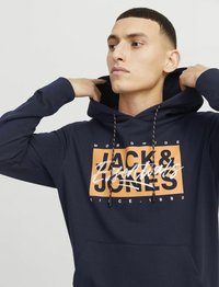 Navy plavi dukserica izrađena od mekanog materijala, s narančastim grafičkim otiskom s natpisom "Jack & Jones" i vezicama s crnim akcentima.
