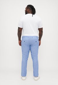 Lyseblå, teksturerte bukser med slim fit, to baklommer, iført en hvit kortermet skjorte og nøytrale joggesko.