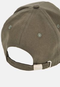 Cappellino da baseball verde oliva con tessuto testurizzato, cinturino regolabile sul retro e occhielli di ventilazione cuciti. Dettaglio in metallo liscio con fibbia.