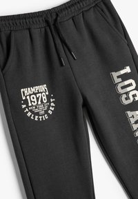 Pantalones de chándal negros con cinturilla elástica, cordón y estampados gráficos: "Campeones 1978 Departamento Atlético" en una pierna y "Los Ángeles" en la otra.