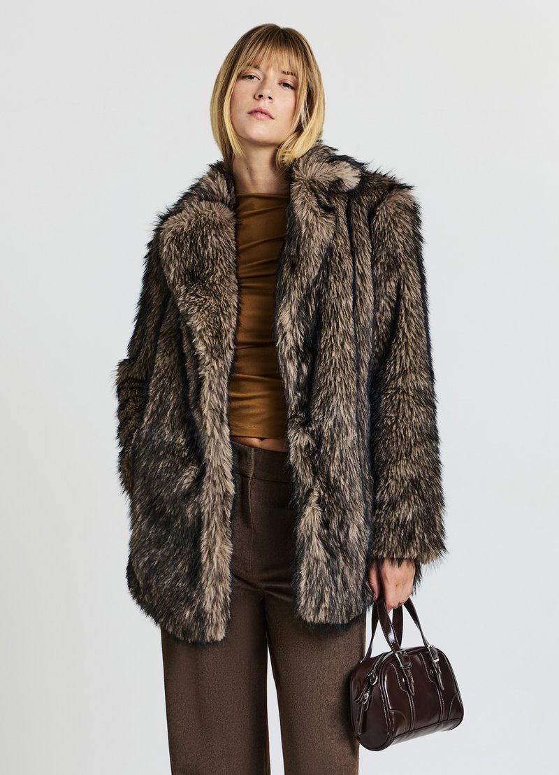 Cappotto in pelliccia sintetica nei toni marroni e grigi, con un ampio colletto e maniche lunghe. Design testurizzato a metà lunghezza. Abbinato a una borsa scura.