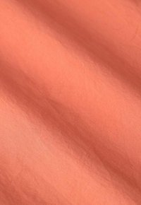 Tissu doux et léger dans une couleur corail pâle avec une texture lisse et un éclat subtil, présentant de légères plis et froissements.