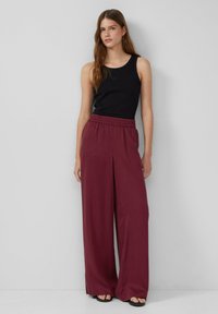 Schwarzes Tanktop mit Rundhalsausschnitt, kombiniert mit weiten burgunderfarbenen Hosen mit elastischem Bund. Glatte Stoffoberfläche.