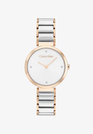 Montre Calvin Klein avec un boîtier rond en argent et or rose, cadran blanc avec quatre accents et un bracelet en maillons métalliques.