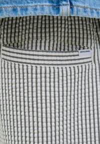 Podszewka kieszeni w paski z czarno-białymi pionowymi liniami, z przyszytą etykietą z napisem "JACK & JONES." Materiał wydaje się być teksturowany.
