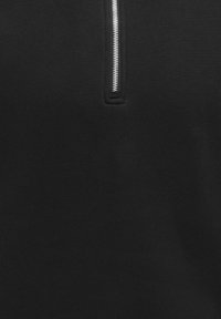 Tissu noir avec une fermeture éclair en métal argenté centrée, partiellement ouverte, montrant une couture fine autour de la zone de la fermeture éclair.