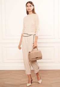 Un pull léger beige et un pantalon sur mesure associés à un sac à main structuré en cuir croco beige et des escarpins à bouts pointus.