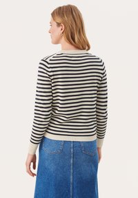 Maglione a righe in crema e navy, con scollatura rotonda e polsini a costine. Abbinato a una gonna di denim blu con tasche posteriori.