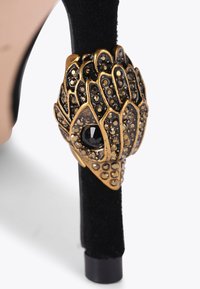 Scarpa con tacco alto nera, realizzata con una parte superiore in tessuto nero testurizzato. Presenta un'inserzione in tono oro con pietre nere e dorate sul tacco.