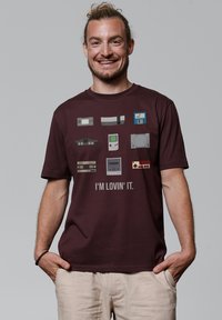 T-shirt bordeaux avec des graphiques de console de jeu rétro et le texte "JE L'AIME." Manches courtes et encolure ronde. Tissu léger.