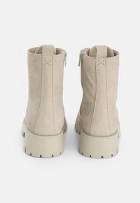 Bottines en daim beige avec un bout arrondi et une semelle crantée épaisse de couleur beige clair. Dotées de fermetures éclair des deux côtés et de détails de coutures visibles.
