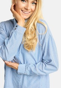 Mėlyna ir balta dryžuota mygtukais užsegama ilgomis rankovėmis marška, pasižyminti laisvu siluetu, rankogalių detalėmis ir smulkiais taškeliais ant audinio.