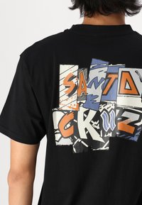 Schwarzes Baumwoll-T-Shirt mit einem mehrfarbigen grafischen Design auf der Rückseite, das auffällige, vielfältige Typografie sowie eine Mischung aus Texturen und Mustern zeigt.