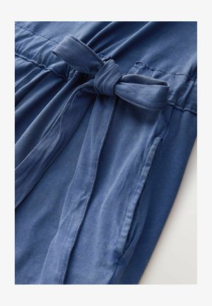 Rochie din țesătură albastră, cu talie legată, strângere elastică și buzunare laterale. Textura este netedă, cu un luciu subtil.