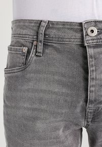 Grå denimjeans med en klassisk femficksdesign, metallknappstängning och subtil texturerad yta.