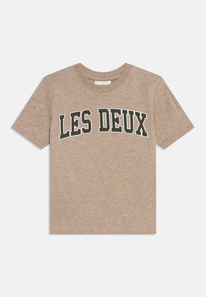 Beige T-shirt met korte mouwen met zwarte en witte vetgedrukte tekst "LES DEUX" over de borst op een effen achtergrond.