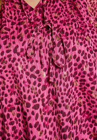 Blusa rosa con un motivo a stampa leopardata, caratterizzata da macchie bordeaux scure e dettagli dorati. Progettata con un nodo nella scollatura e una texture plissettata.